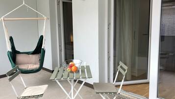 A balcony with a hanging chair, a table with chairs, and a fruit bowl.