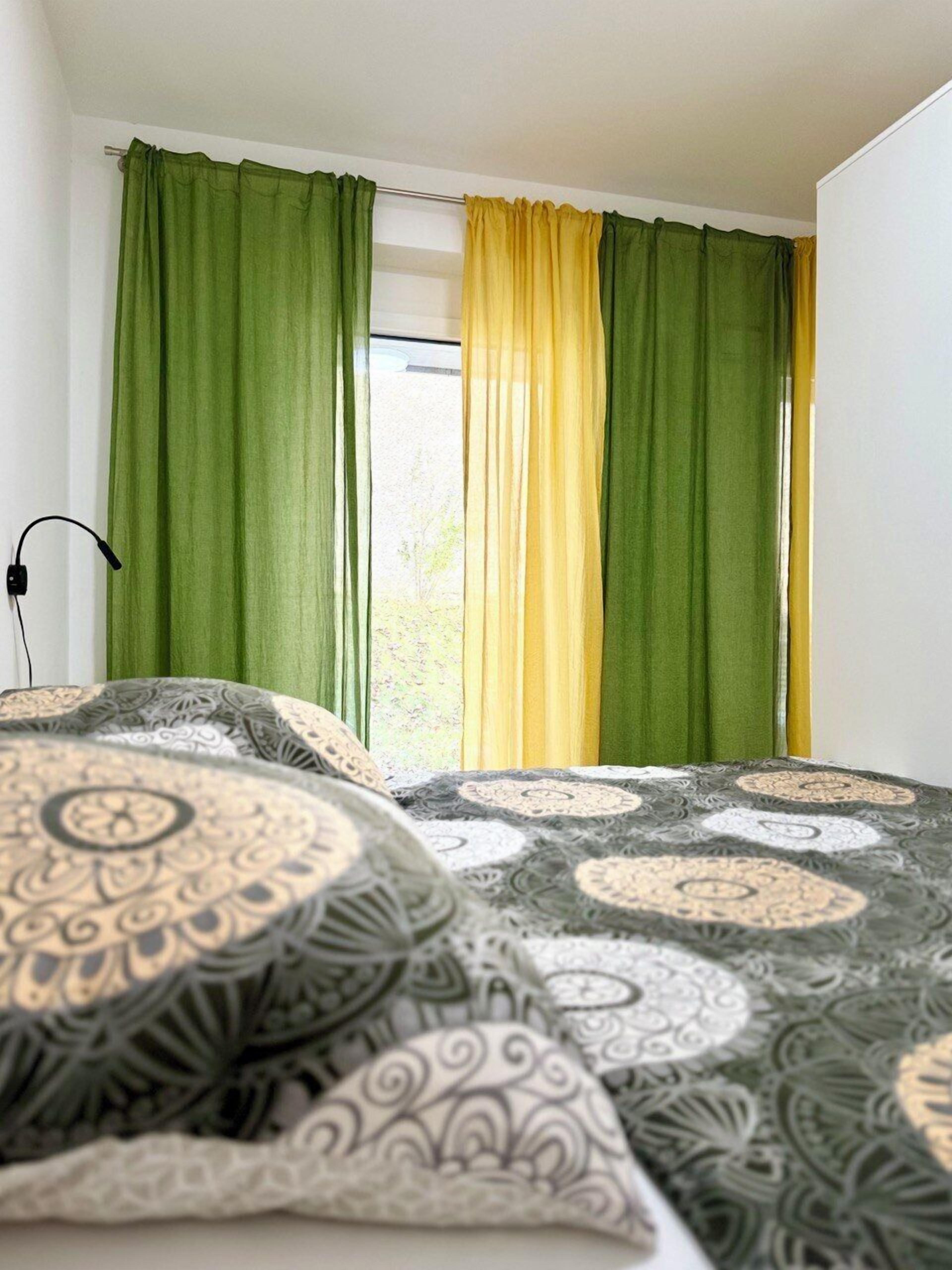 Una camera da letto con un letto, tende verdi e gialle, e biancheria da letto decorata.