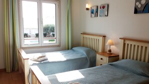 Une chambre avec deux lits, une fenêtre, une lampe et des œuvres d’art accrochées au mur.