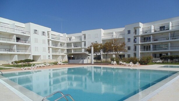 Un bâtiment moderne doté d’une piscine, de nombreux balcons et de chaises longues.
