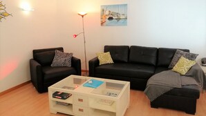 Un salon avec deux canapés noirs, une table basse blanche et un lampadaire. Un tableau est accroché au mur et un climatiseur est installé au-dessus du canapé.