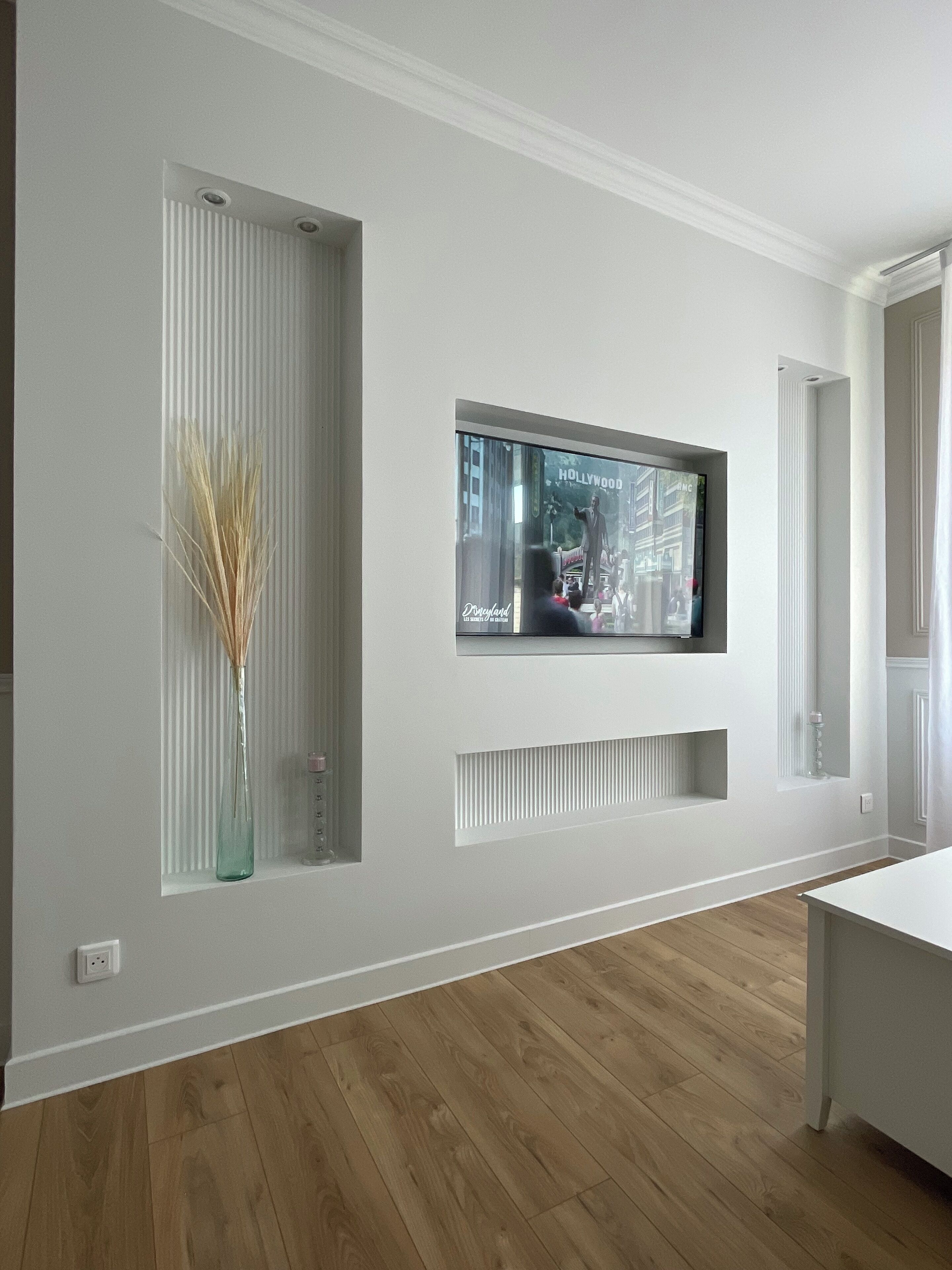 Une chambre moderne avec un grand téléviseur fixé au mur, un plancher en bois et un plafond blanc.