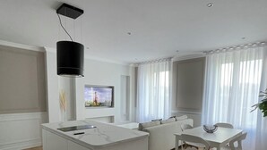 Une cuisine moderne dotée d’un îlot central, de meubles blancs et d’un téléviseur à écran plat fixé au mur.