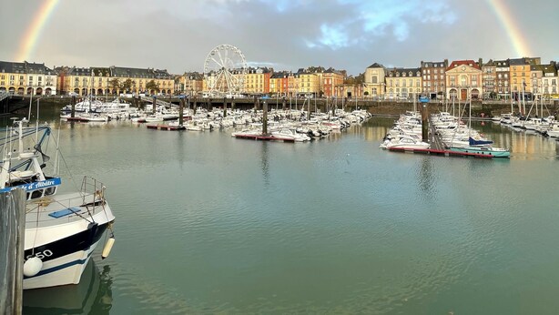 Un port de plaisance avec des bateaux amarrés, une grande roue et des bâtiments en arrière-plan.