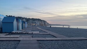 Une promenade en bois qui mène à des cabanes de plage le long d’une côte de galets.