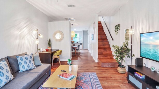 A modern living room with a sofa, coffee table, TV, and staircase leading to another room. - The Prairie at Brighton | UF • Pool • Workspace (Gainesville)