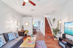 A modern living room with a sofa, coffee table, TV, and staircase leading to another room. - The Prairie at Brighton | UF • Pool • Workspace (Gainesville)