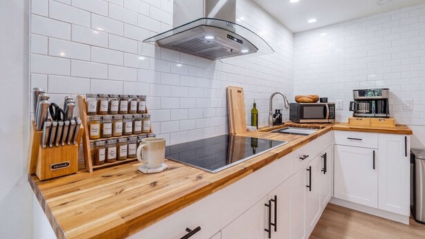 A modern kitchen with white tiled walls, a wooden countertop, a built-in microwave, and a variety of kitchen utensils and appliances.