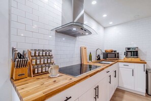 Une cuisine moderne avec des murs recouverts de carreaux blancs, un plan de travail en bois, un four à micro-ondes encastré, ainsi qu’une variété d’ustensiles et d’appareils de cuisine.