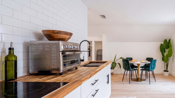 Une cuisine moderne dotée d’un four encastré, d’un saladier en bois posé sur le plan de travail, et d’un coin repas avec une table ronde et des chaises.