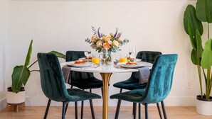 Un coin repas avec une table ronde, des chaises de couleur turquoise et un centre de table floral.