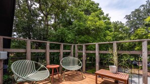 Une terrasse en bois avec deux chaises et une table, entourée d’une clôture en bois et d’une végétation luxuriante.