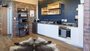 Una cocina moderna con armarios blancos, una pared de ladrillo decorativa y un estante colgante con utensilios de cocina.