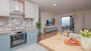A modern kitchen with a built-in oven, a dining area with a wooden table, and a balcony with a view.