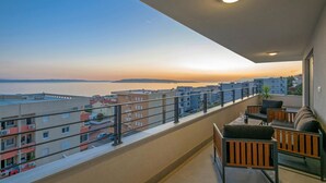 A balcony with a view of the sea and buildings during sunset.