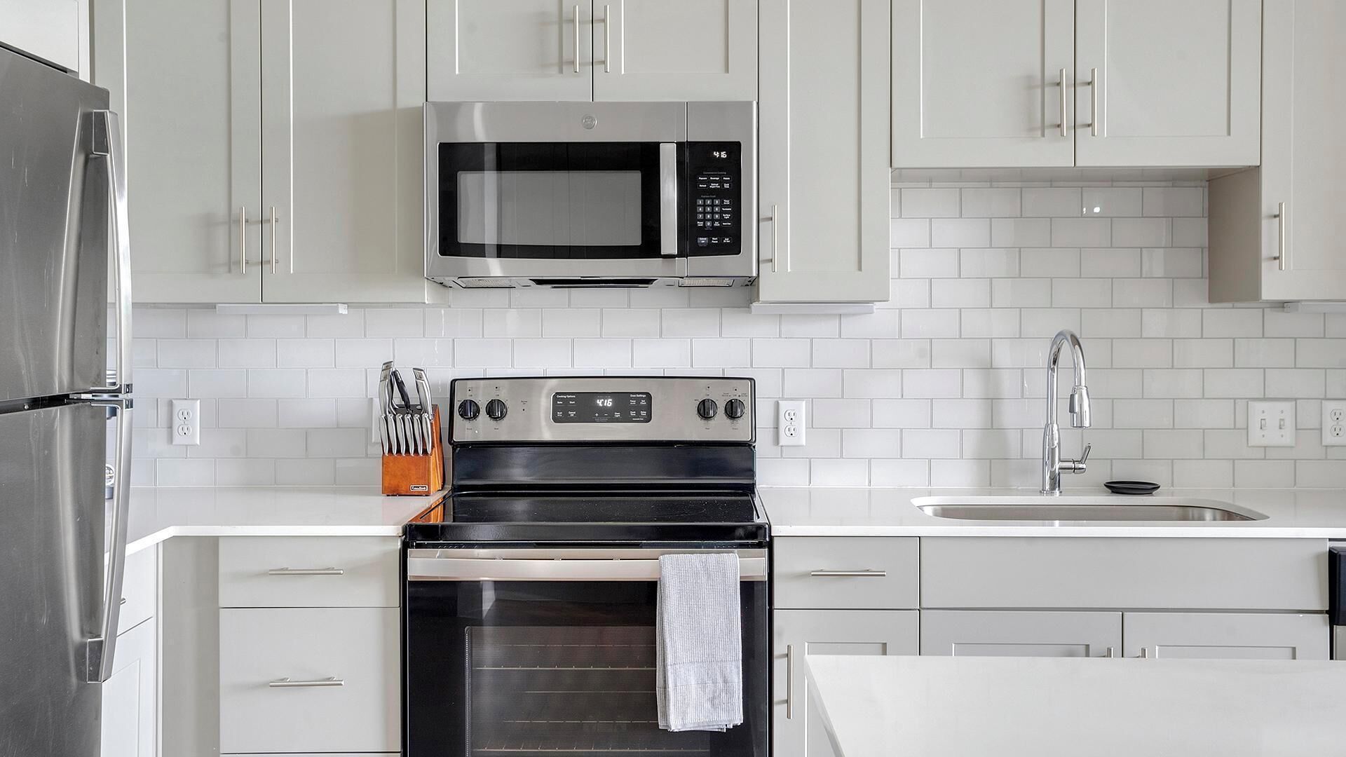 Una cocina moderna con armarios blancos, un refrigerador de acero inoxidable, un microondas, un horno y un lavamanos con grifo.