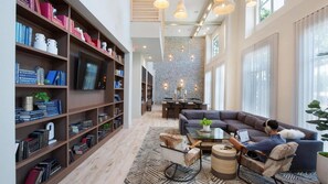 A spacious living area with a large bookshelf, a comfortable sofa, and a dining area with a stone wall. - Landing | Chic 2BD, Pool, Courtyard (Austin)