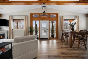 Amplia sala de estar con chimenea, comedor con mobiliario de madera y una puerta de madera grande que da al exterior.