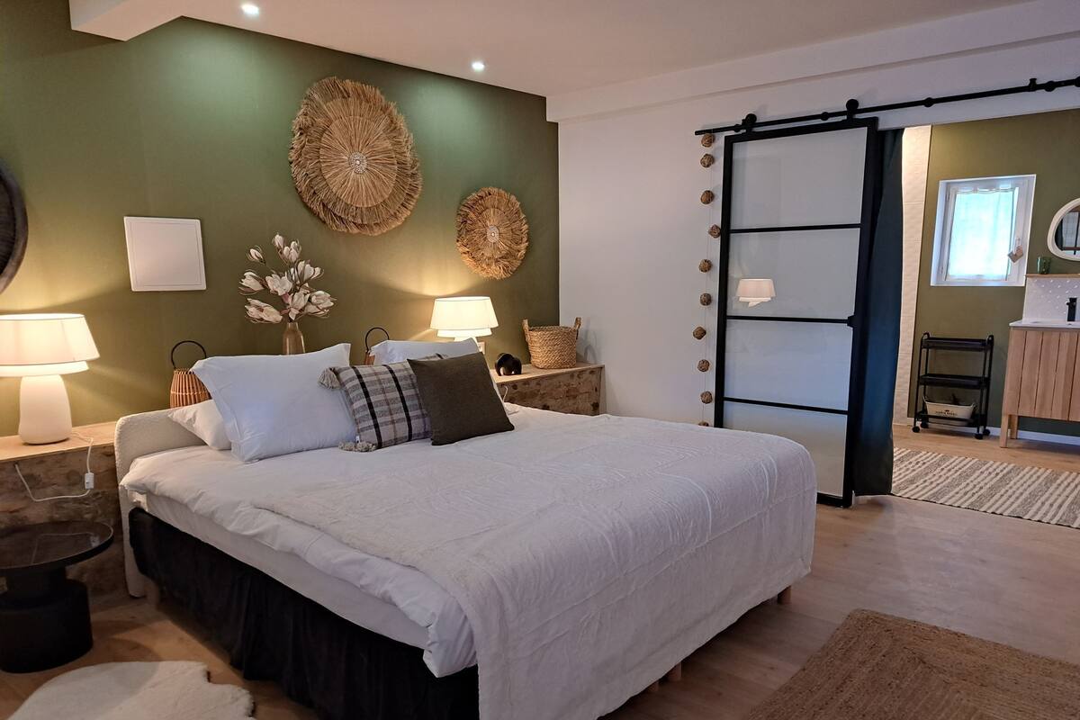 A modern bedroom with a large bed, two bedside tables, wall art, and a sliding door leading to a bathroom.