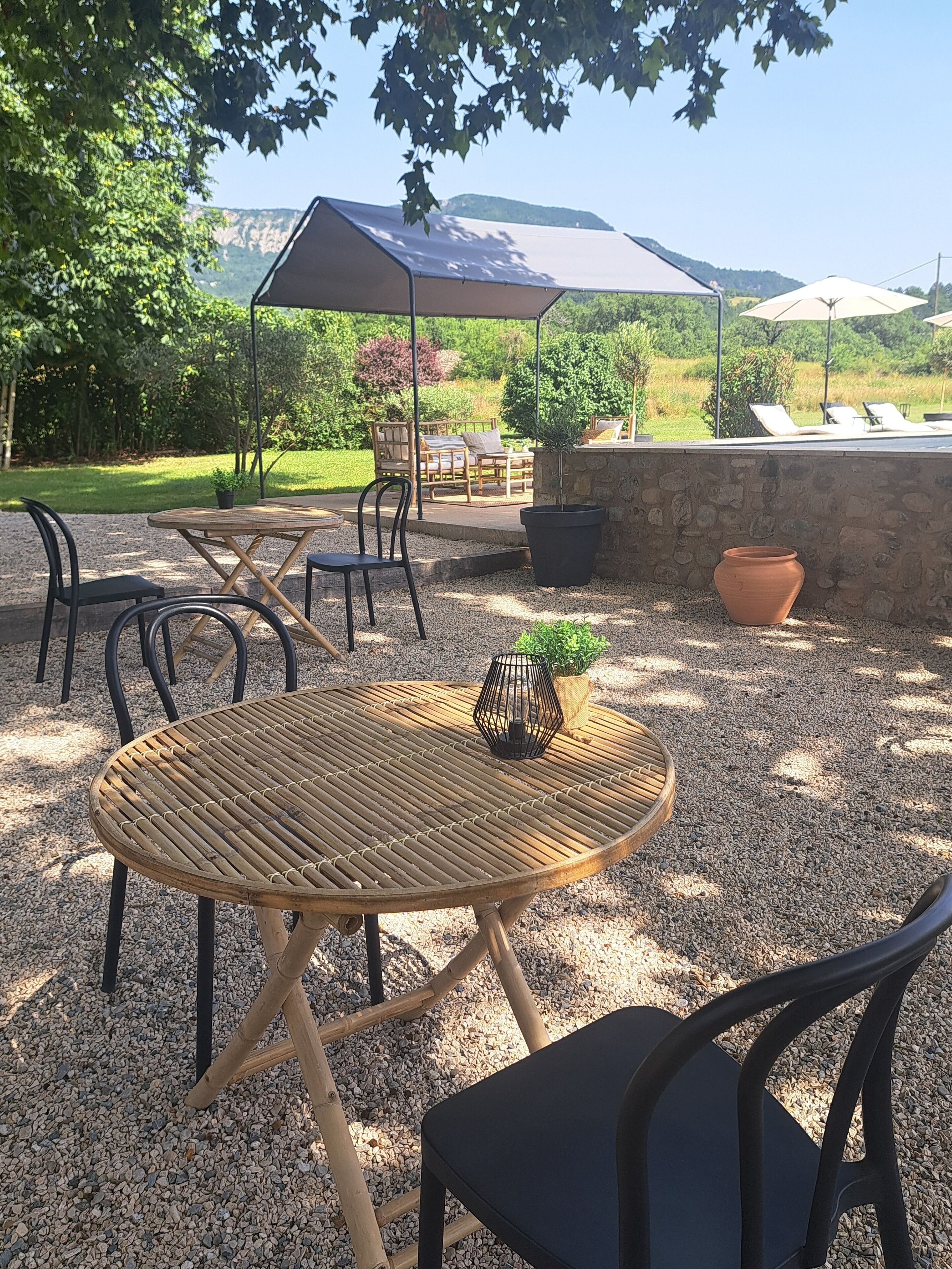 A round table with chairs, a stone wall, and a view of a grassy area with trees and a mountain in the background.