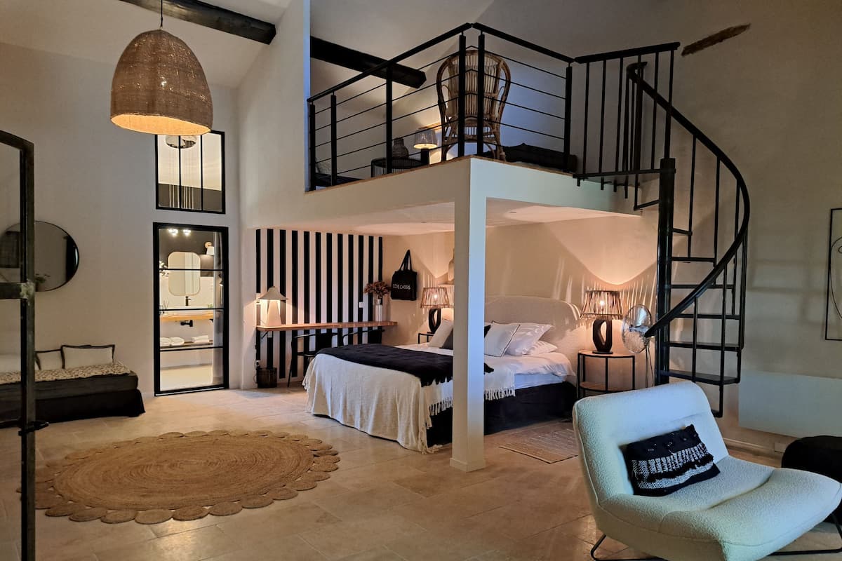 A modern bedroom with a bed, bedside tables, a chair, a staircase, and a hanging light fixture.