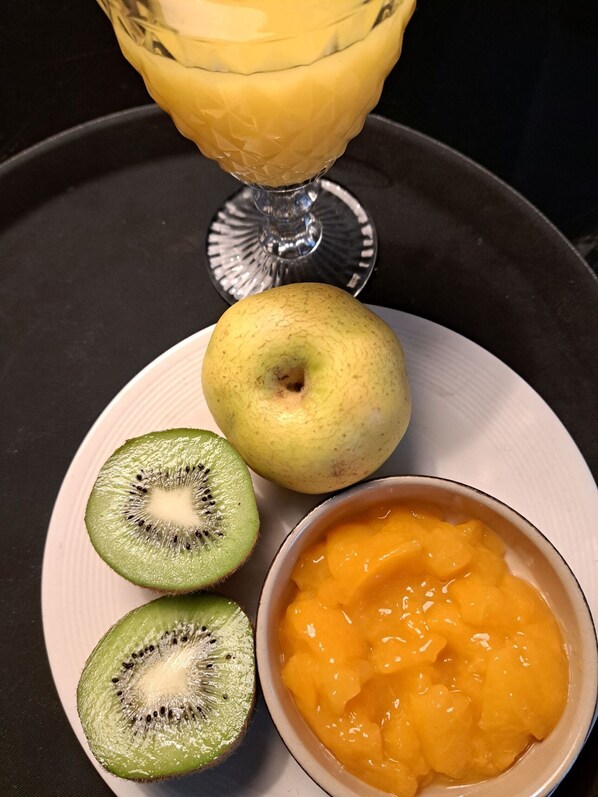 Un plato con una manzana entera, dos mitades de kiwi y un cuenco con puré de melocotón.