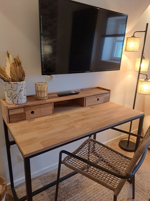 Un escritorio de madera con un televisor encima, una silla de mimbre y una lámpara a la derecha.