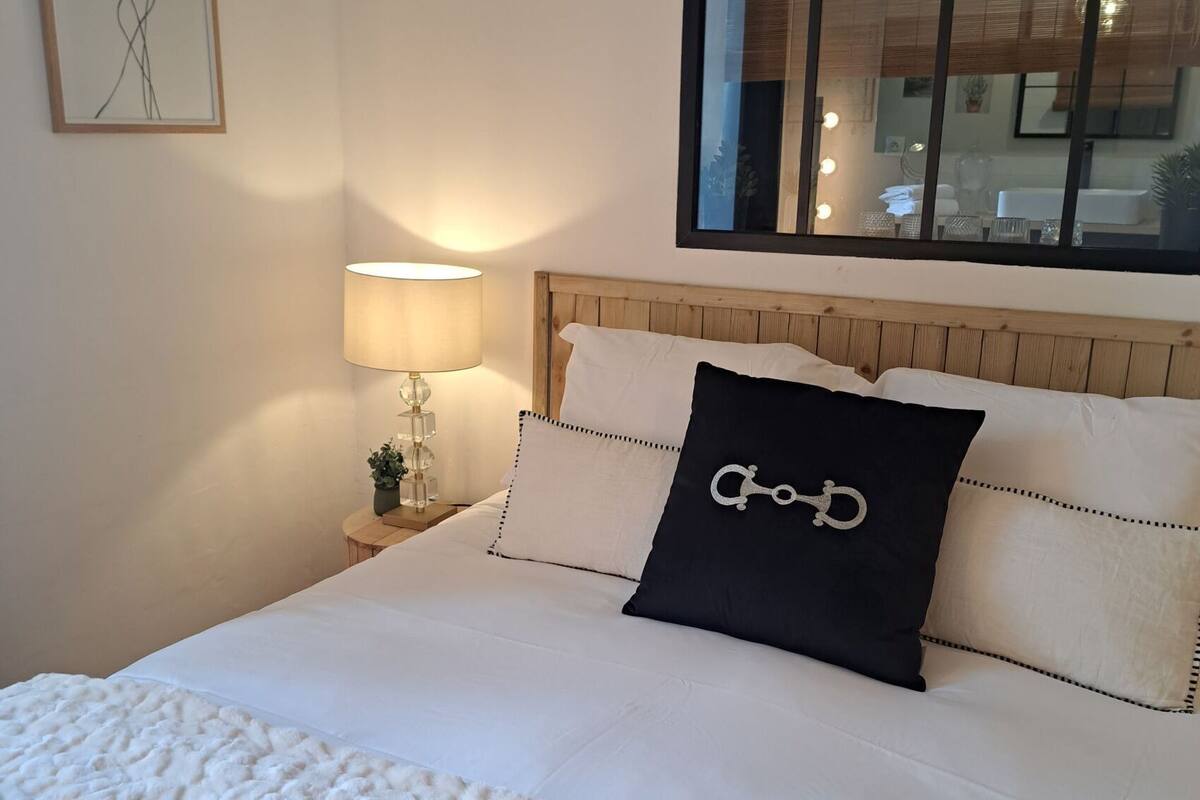 A neatly made bed with a white quilt, a black pillow with a keychain, and a bedside lamp.