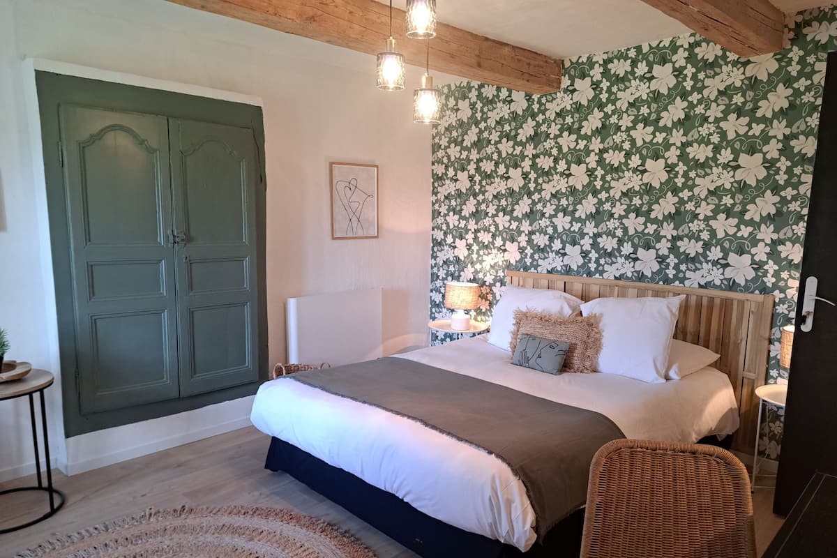 A bedroom with a large bed, a wooden headboard, a green door, a floral wallpaper, and a round rug.