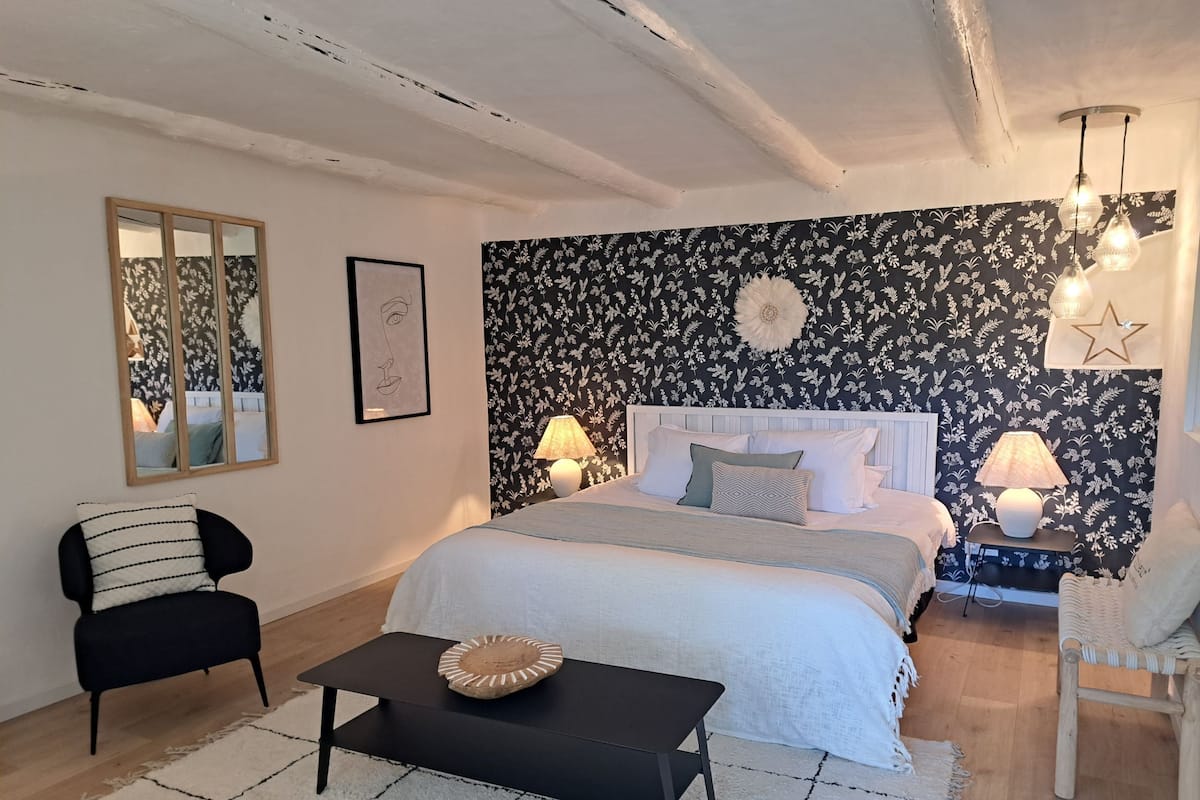 A bedroom with a bed, bedside lamps, a mirror, a chair, and a small table.