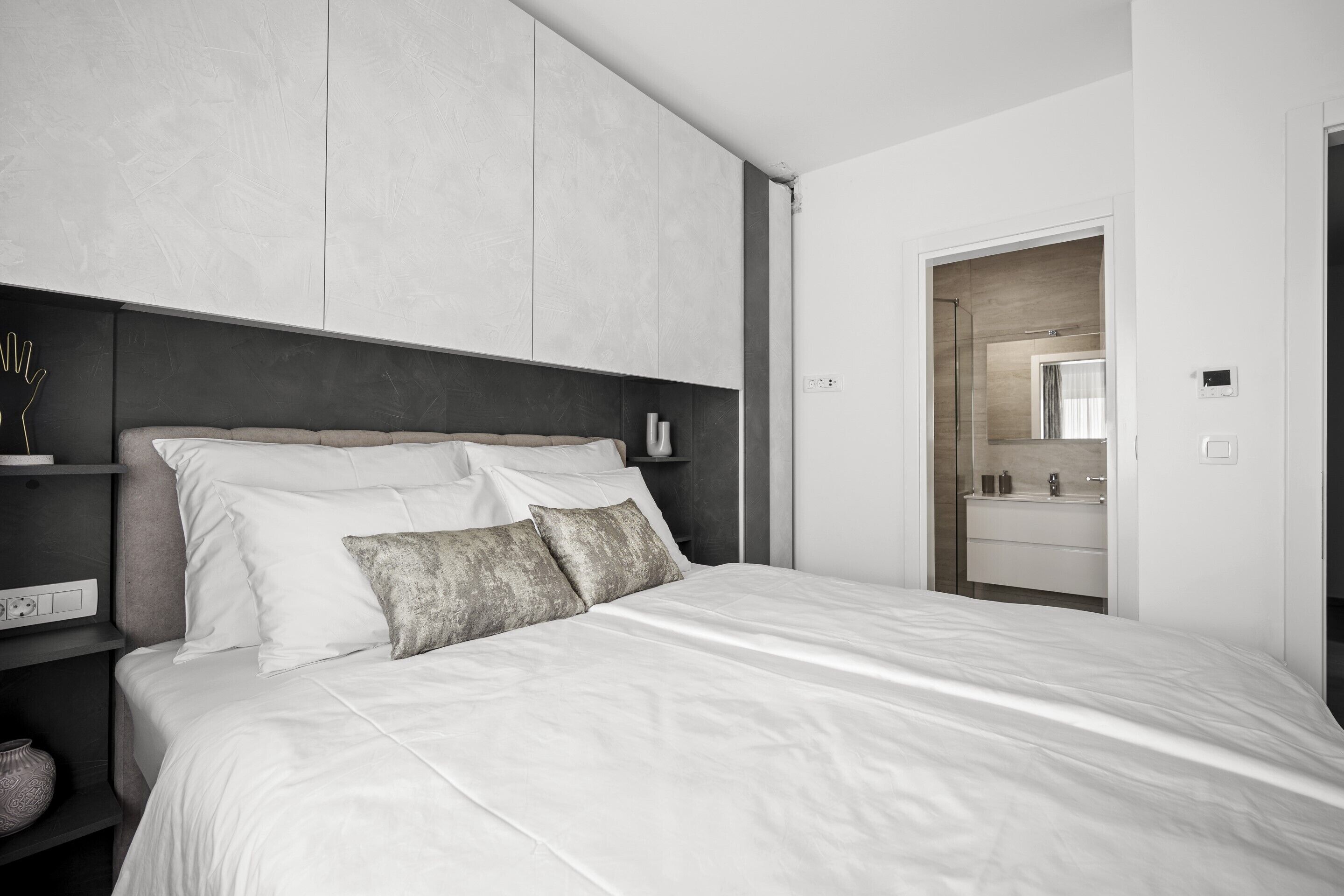 Quarto moderno com uma cama grande, mesa de cabeceira com abajur e guarda-roupa.