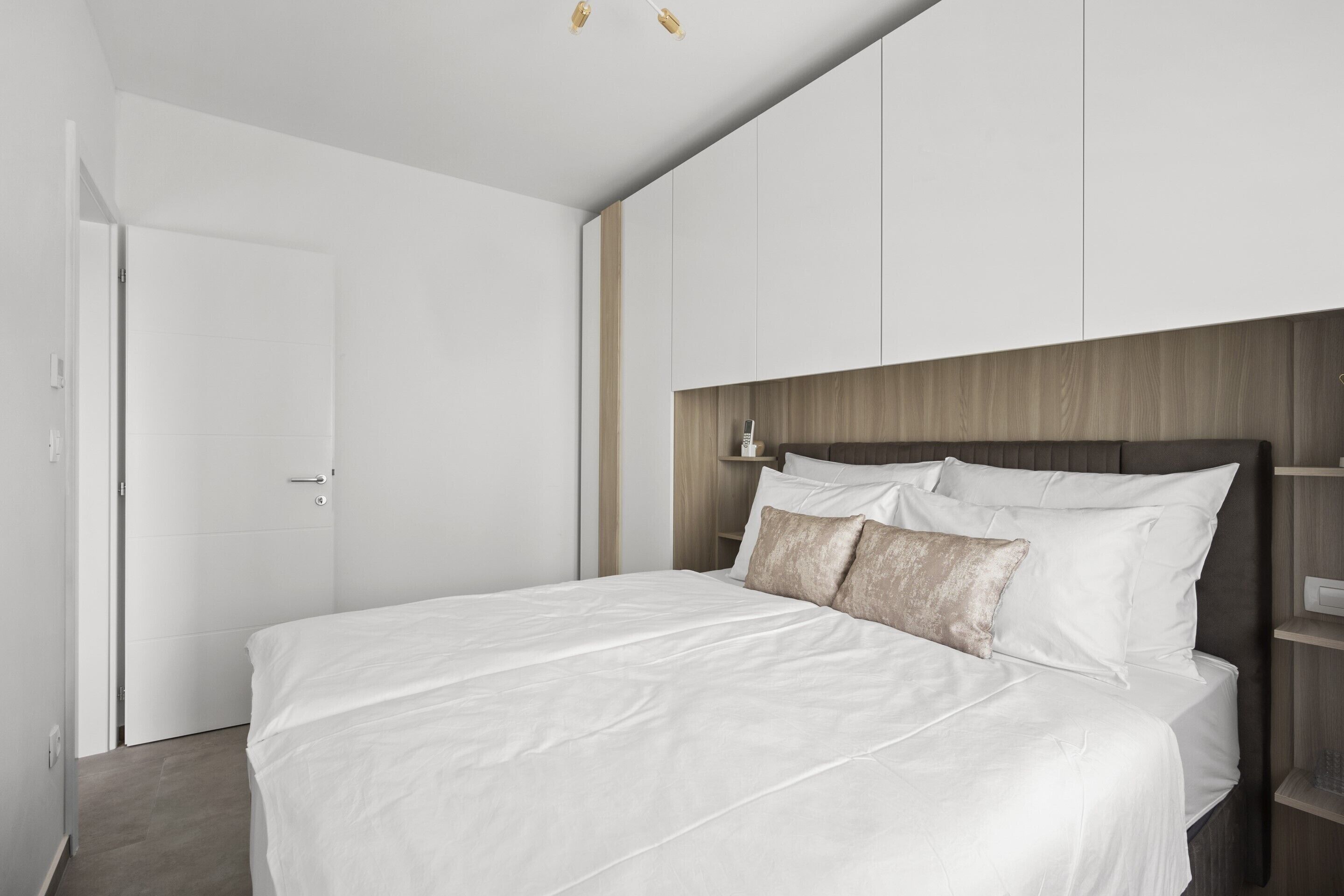 Ein modernes Schlafzimmer mit einem großen Bett, einem Holz-Kopfteil und weißen Wänden.