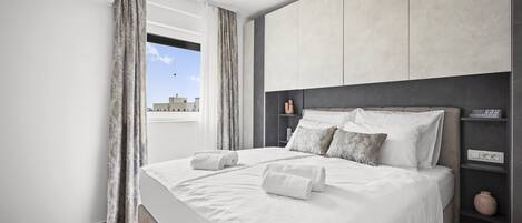 Un dormitorio moderno con una cama grande, cabecera, mesita de noche y ventana con cortinas.