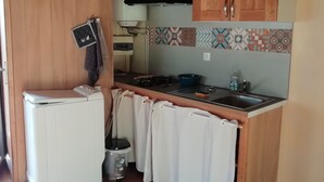 A compact kitchen with wooden cabinets, a built-in stove, and a small sink. - Petit Chalet Pentagonal Entre Prés et Forêt (Merlas)