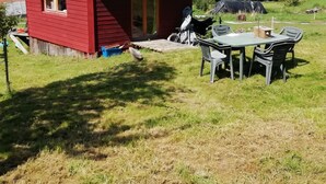 A small red wooden house with a sloped roof, a porch, and a table with chairs outside. - Petit Chalet Pentagonal Entre Prés et Forêt (Merlas)