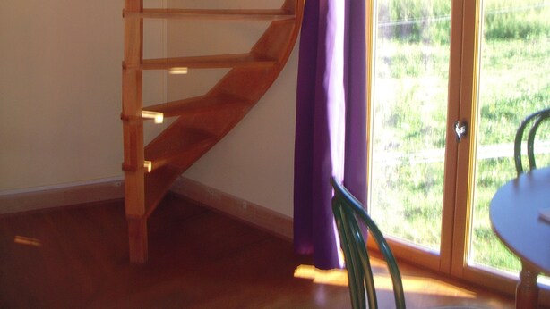 A wooden spiral staircase in a room with a large window and a door leading outside. - Petit Chalet Pentagonal Entre Prés et Forêt (Merlas)