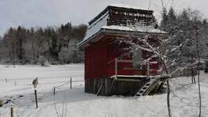 A red wooden cabin with a snow-covered roof and a wooden staircase leading up to a door. - Petit Chalet Pentagonal Entre Prés et Forêt (Merlas)