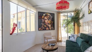 A living room with a green sofa, a round wooden coffee table, and a beige armchair. There is a large painting on the wall and a red hanging light fixture. - Casa Rosa: Long-term Living & Workspace (Valencia)