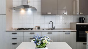 A modern kitchen with white cabinets, a stainless steel range hood, a gas stove, a sink, and a coffee maker. - Villa Karibu in Cicirata (Avola)