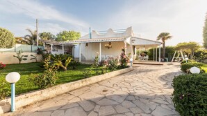 A house with a patio area, a covered outdoor seating space, and a garden with various plants and flowers. - Villa Karibu in Cicirata (Avola)