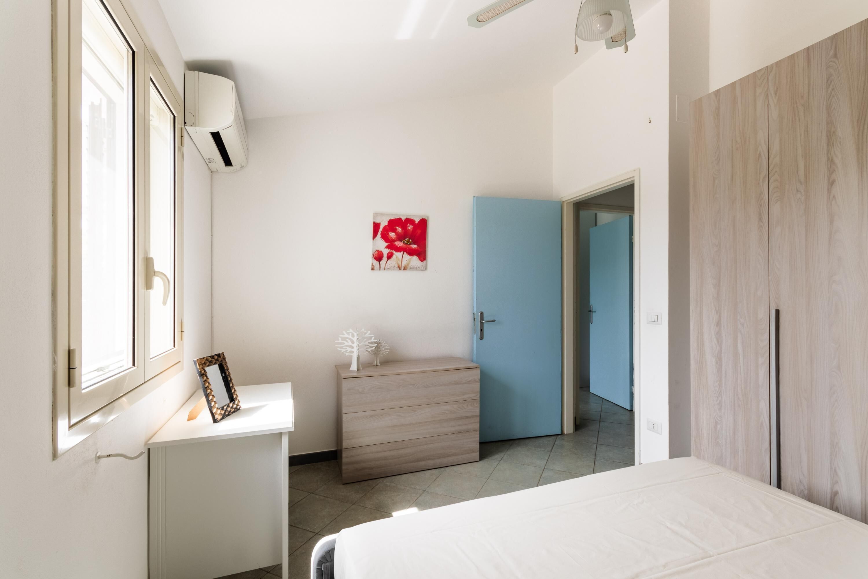 A bedroom with a bed, a dresser, a blue door, and a wall-mounted air conditioner.