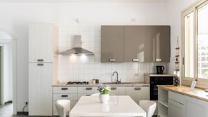 A modern kitchen with white cabinetry, a gas stove, and a white dining table with chairs. - Villa Karibu in Cicirata (Avola)
