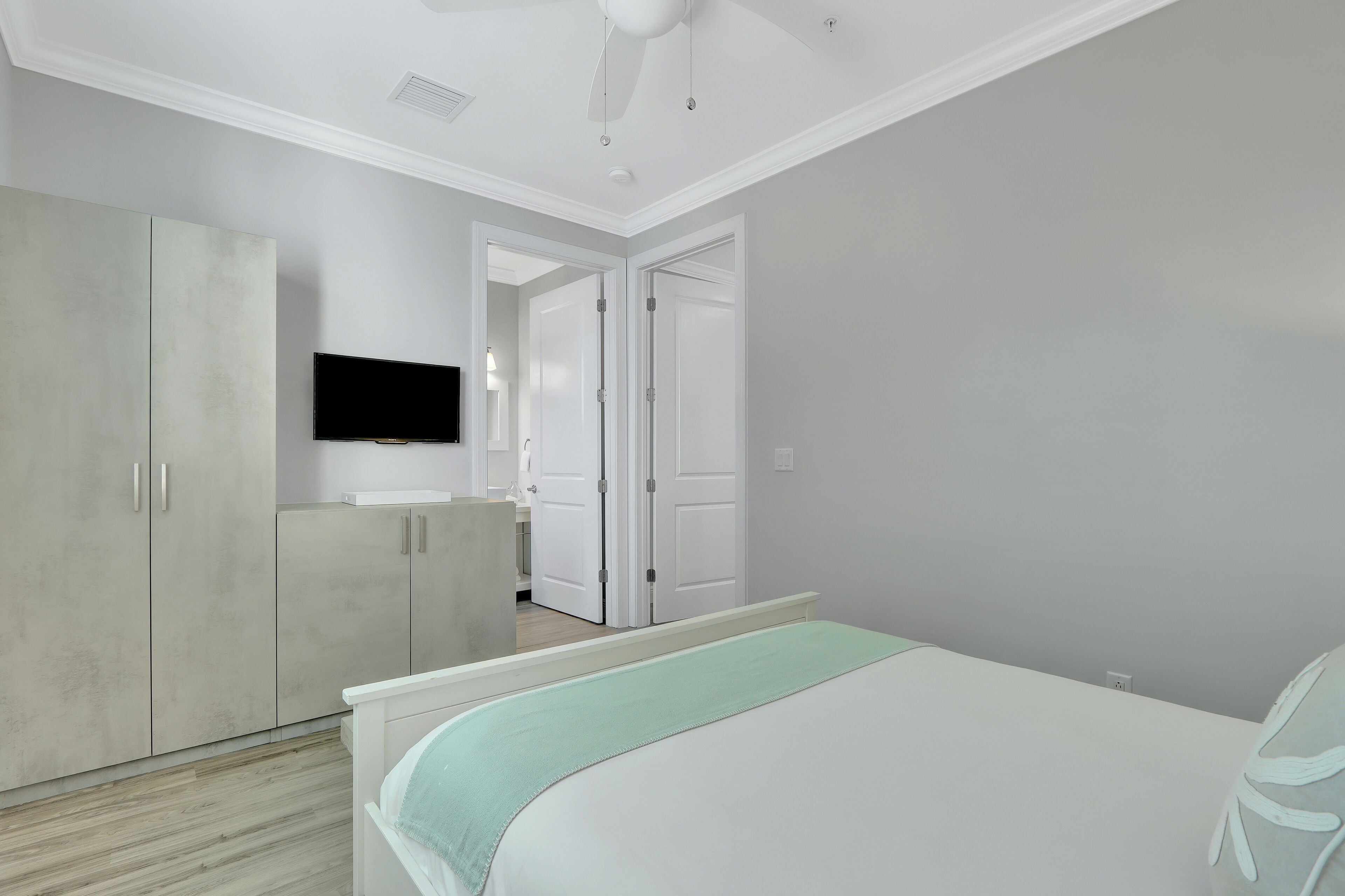 A bedroom with a bed, a wardrobe, a television, and a door leading to another room.