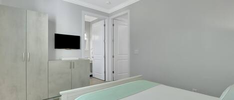 A bedroom with a bed, a wardrobe, a television, and a door leading to another room.