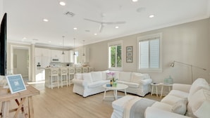 A spacious living room with a white sofa set, a coffee table, and a dining area with white cabinets and a kitchen in the background. - Isla Key Lime: Boutique Resort, FREE Boat Dockage Sept-Oct Only! (Islamorada)