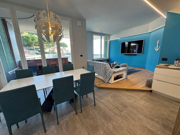 A modern dining area with a table and chairs, a sofa, a TV, and a view of the outdoors.