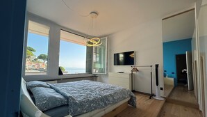 A bedroom with a bed, a TV, a window with a view, and a ceiling light. - La Soluzione Perfetta (Arenzano)