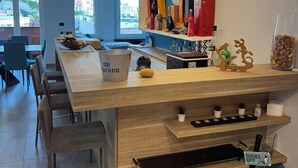 A modern bar area with a wooden counter, bar stools, and a variety of bottles and decorative items. - La Soluzione Perfetta (Arenzano)