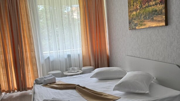 A modern hotel room with a large bed, white linens, a painting on the wall, and sheer curtains. - Legacy Hotel (Eforie)