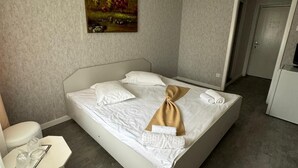 A neatly made bed with white linens and a brown towel, a painting of a landscape on the wall, and a small table with glasses and a book. - Legacy Hotel (Eforie)